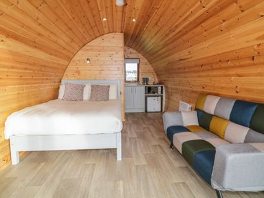 A wooden pod room with a bed pillows a patchwork sofa and a kitchenette at The Wheelhouse Pod No 2 in Burtonport County Donegal
