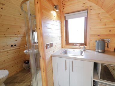 A kitchenette with a sink and kettle next to a small bathroom with a shower in a wooden interior at The Wheelhouse Pod No 2 Burtonport County Donegal