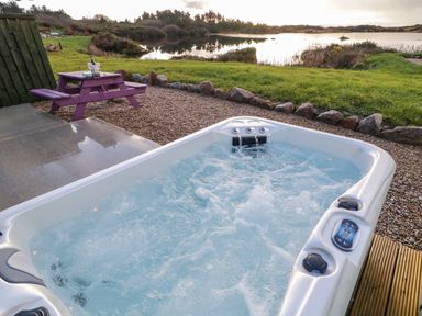 An outdoor hot tub with bubbling water near a purple picnic table and a lake at The Wheelhouse Pod No 2 in Burtonport County Donegal