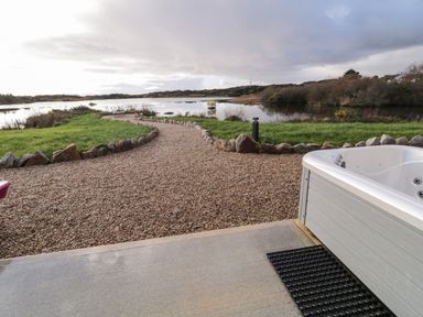 A gravel pathway bordered by stones leading to a lake with a boat and surrounding greenery at The Wheelhouse Pod No 2 in Burtonport County Donegal