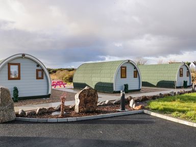 Three curved pods with green roofs and white walls near a stone sign that reads pods at The Wheelhouse Pod No 2 Burtonport County Donegal
