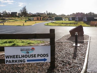 Outdoor parking area with small pod-style cabins and a wooden sign pointing to Wheelhouse Pods parking at The Wheelhouse Pod No 2 Burtonport County Donegal