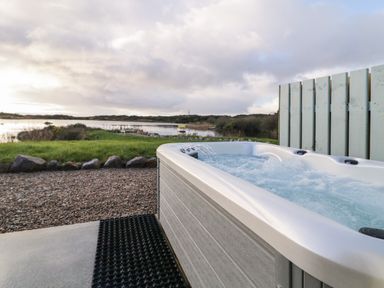 An outdoor hot tub near a gravel path with a lake and grassy area in the background at The Wheelhouse Pod No 3 in Burtonport County Donegal
