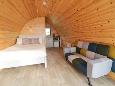 A wooden pod interior with a bed a colorful patchwork sofa and a small kitchenette at The Wheelhouse Pod No 3 Burtonport County Donegal