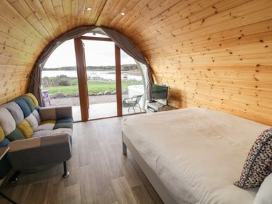 A bedroom with a bed sofa and television overlooking a lake at The Wheelhouse Pod No 3 in Burtonport County Donegal