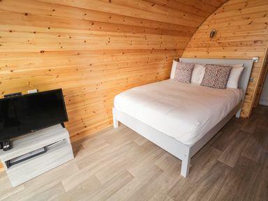 A bedroom with a bed and two pillows and a TV on a stand against a wooden wall at The Wheelhouse Pod No 3 Burtonport County Donegal