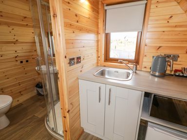 A small kitchen area with a sink kettle and microwave next to a bathroom with a toilet and shower at The Wheelhouse Pod No 3 Burtonport County Donegal