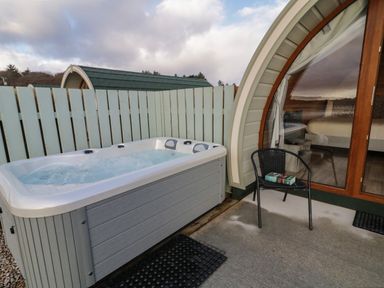 An outdoor hot tub next to a black chair with a book on it outside a pod with a glass door at The Wheelhouse Pod No 3 Burtonport County Donegal