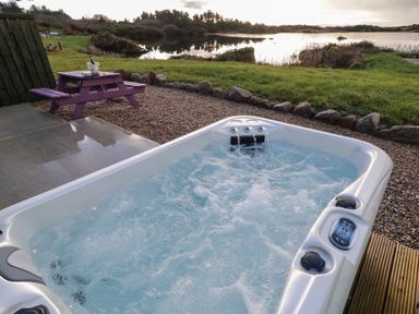 An outdoor hot tub with water jets near a purple picnic table by a lake at The Wheelhouse Pod No 3 Burtonport County Donegal