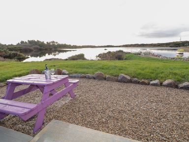 A purple picnic table with a wine bottle and glasses near a lake and grassy area at The Wheelhouse Pod No 3 Burtonport County Donegal