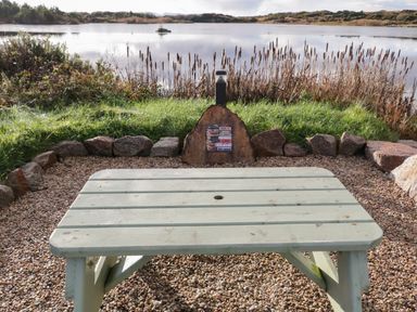 A picnic table facing a lake with reeds and rocks at The Wheelhouse Pod No 3 Burtonport County Donegal