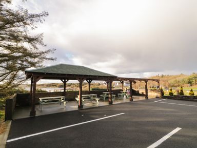 A covered outdoor seating area with picnic tables next to a parking lot at The Wheelhouse Pod No 3 in Burtonport County Donegal