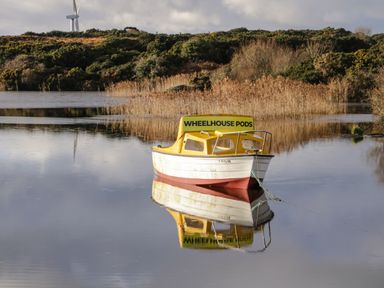 A small boat on calm water with reed beds and bushes in the background at The Wheelhouse Pod No 3 in Burtonport County Donegal
