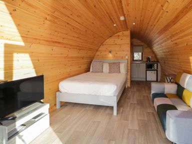 A wooden pod interior with a bed, a television, a sofa, and a kitchenette at The Wheelhouse Pod No 4 in Burtonport County Donegal