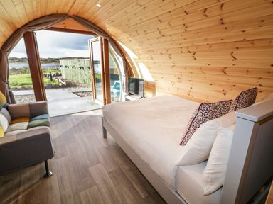 A wooden interior room with a bed and a sofa near an open door looking outside at The Wheelhouse Pod No 4 in Burtonport County Donegal