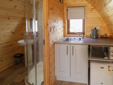 A small kitchen area with a sink microwave fridge and kettle next to a bathroom with shower and sink at The Wheelhouse Pod No 4 in Burtonport County Donegal