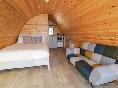 A wooden pod interior with a bed and pillows a small kitchenette and a multicolored sofa at The Wheelhouse Pod No 7 in Burtonport County Donegal