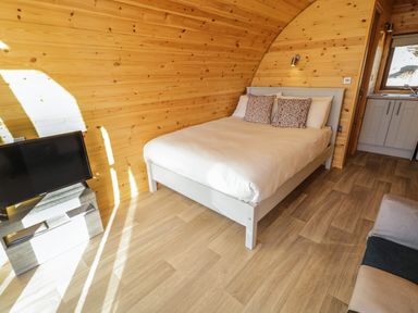A bedroom with a bed two pillows a TV on a stand and a doorway to a kitchen at The Wheelhouse Pod No 7 Burtonport County Donegal