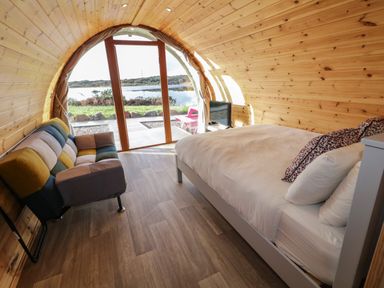 A pod interior with a bed sofa and television facing glass doors showing outdoor water view at The Wheelhouse Pod No 7 Burtonport County Donegal