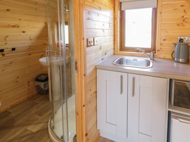 A kitchen sink and counter next to a shower with a sink and trash can in a wood paneled room at The Wheelhouse Pod No 7 in Burtonport County Donegal