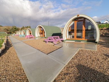 A row of pod cabins with glass doors and colored picnic tables on a gravel surface at The Wheelhouse Pod No 7 in Burtonport County Donegal