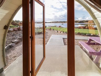 A view through glass doors opening to a patio with a purple picnic table and a pathway leading to a lake at The Wheelhouse Pod No 9 Burtonport County Donegal