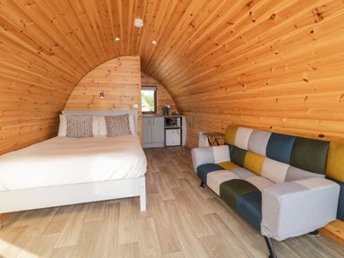 A small room with a bed, colorful sofa, kitchenette, and wooden curved walls at The Wheelhouse Pod No 9 in Burtonport County Donegal