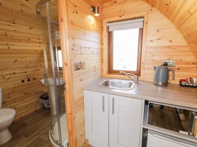 A compact kitchen and bathroom area with wooden walls a sink a kettle a microwave a shower and a toilet at The Wheelhouse Pod No 9 in Burtonport County Donegal