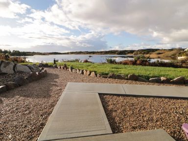 A gravel pathway with a stone border leading to a body of water with green grass and shrubs around at The Wheelhouse Pod No 9 in Burtonport County Donegal