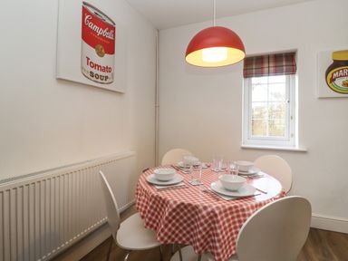 A dining area with a round table covered by a red and white checkered tablecloth set for four with bowls and glasses at The Little White Cottage in Milton-Under-Wychwood