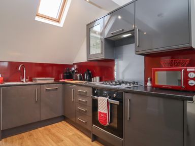 A kitchen with grey cabinets red backsplash wooden floor and a skylight at The Little White Cottage in Milton-Under-Wychwood