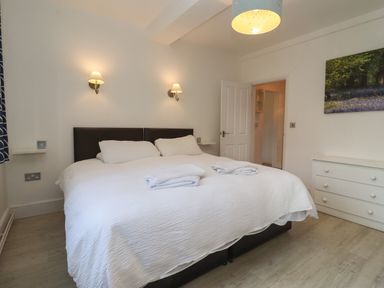A bedroom with a double bed two wall lamps a white chest of drawers and a door at The Little White Cottage in Milton-Under-Wychwood