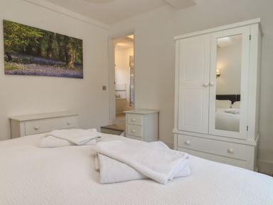 A bedroom with a bed with folded towels a white wardrobe and a small dresser at The Little White Cottage in Milton-Under-Wychwood