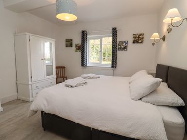 A bedroom with a double bed white wardrobe wooden chair and window with curtains at The Little White Cottage in Milton-Under-Wychwood
