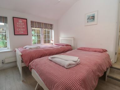 A bedroom with two single beds with red checkered bedding and two folded white towels a framed keep calm and carry on poster and a window with striped blinds at The Little White Cottage in Milton-Under-Wychwood