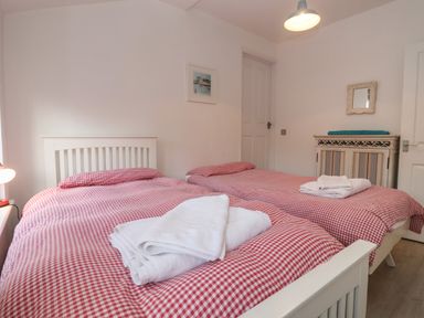 A bedroom with two single beds with red checkered bedding and folded towels on top at The Little White Cottage in Milton-Under-Wychwood