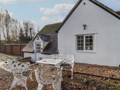 An outdoor seating area with white metal chairs and a table beside a white house with a window and door at The Little White Cottage in Milton-Under-Wychwood