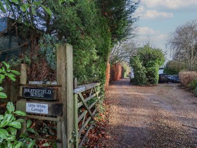 A gravel driveway with parked cars and wooden gate with signs for Heathfield House and Little White Cottage at The Little White Cottage in Milton-Under-Wychwood