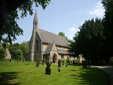 An old stone church with a tall steeple surrounded by gravestones and trees at The Little White Cottage in Milton-Under-Wychwood
