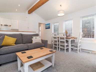 A living room with a gray sofa and a wooden coffee table next to a dining table with white chairs at Bowness Bay Lodge Oakside 16 Fallbarrow Park near Bowness-On-Windermere
