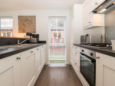 A kitchen with white cabinets black countertops a stainless steel oven a microwave a toaster and a window with blinds at Bowness Bay Lodge Oakside 16 Fallbarrow Park near Bowness-On-Windermere