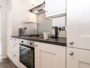 A kitchen with white cabinets a built-in oven a microwave a kettle and a white mug on the counter at Bowness Bay Lodge Oakside 16 Fallbarrow Park near Bowness-On-Windermere