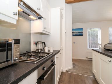 A kitchen with a microwave oven kettle two cups and a gas stove at Bowness Bay Lodge Oakside 16 Fallbarrow Park near Bowness-On-Windermere