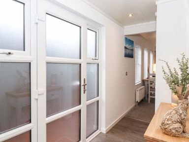 A hallway with frosted glass doors wooden flooring and a wooden side table with a decorative rabbit at Bowness Bay Lodge Oakside 16 Fallbarrow Park near Bowness-On-Windermere