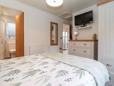 A bedroom with bed, dresser, wall-mounted TV, and door leading to bathroom at Bowness Bay Lodge Oakside 16 Fallbarrow Park near Bowness-On-Windermere