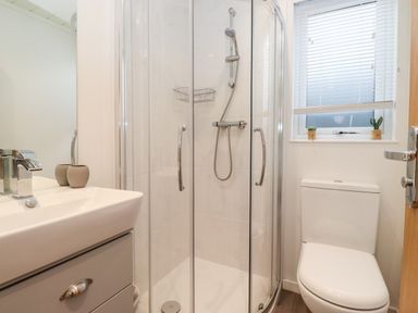 A bathroom with a glass shower enclosure, a sink with a faucet, and a toilet with a window above at Bowness Bay Lodge Oakside 16 Fallbarrow Park near Bowness-On-Windermere