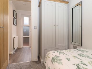 A bedroom with a bed covered in a patterned duvet a white wardrobe and a wall mirror at Bowness Bay Lodge Oakside 16 Fallbarrow Park near Bowness-On-Windermere