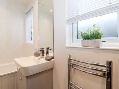 A bathroom with a sink cabinet next to a bathtub and a window with a plant on the sill at Bowness Bay Lodge Oakside 16 Fallbarrow Park near Bowness-On-Windermere