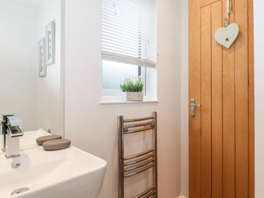 A bathroom with a white sink with a chrome faucet two soap bars a window with blinds and a plant a wooden door and a chrome towel rail at Bowness Bay Lodge Oakside 16 Fallbarrow Park near Bowness-On-Windermere
