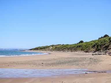 A sandy beach with small waves and green vegetation along the coastline at Valley View Hideaway in Ffostrasol